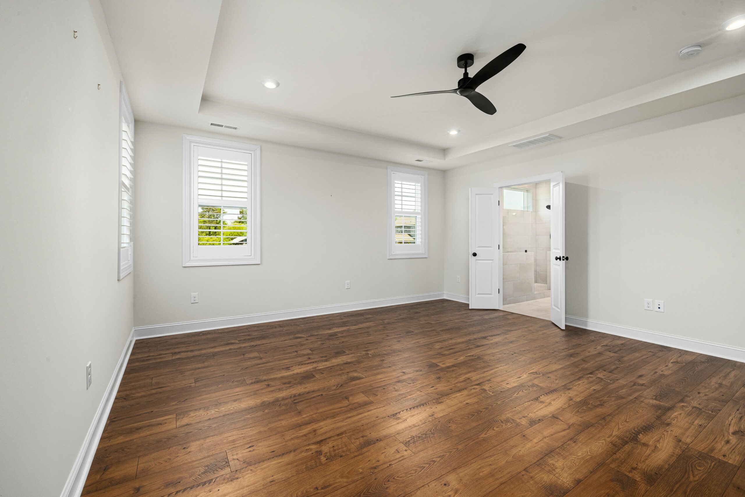 Empty modern bedroom with hardwood floors and ceiling fan, perfect for customization.